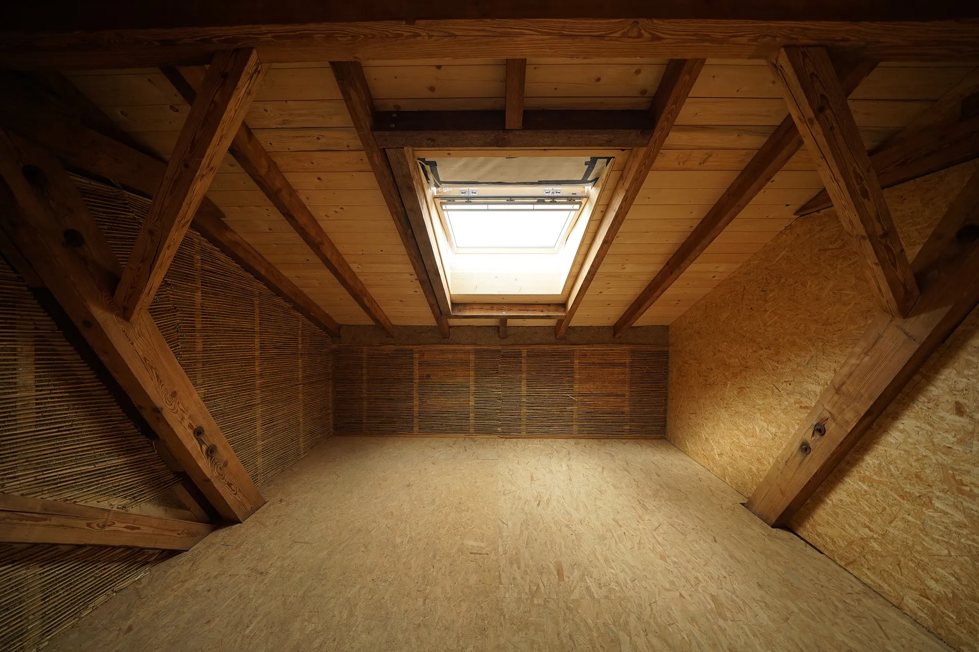 Mit Naturbaustoffen ausgebauter Dachraum: Holzbalken, Schilfrohrdämmung und Oberlicht